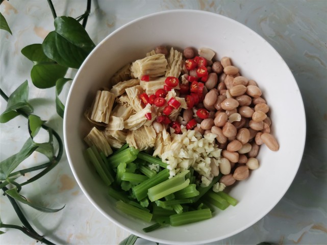 將芹菜,腐竹,煮好的花生米一起放到容器內,淋入炸好的花椒油,再加入蒜