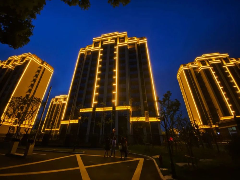 小区淡黄色的外立面上沿着外围镶着灯带,等到夜晚,夜色下明亮大气