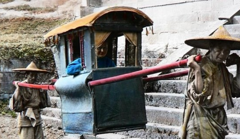 图为两个年纪较大的轿夫抬着一个有钱人家的夫人,轿夫身上的衣服很破