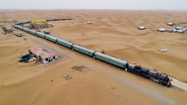 从空中俯视,茫茫腾格里沙漠中,一列充满年代感的蒸汽机绿皮火车蜿蜒"