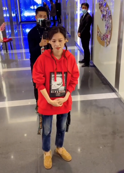 行走在走廊上的张庭穿着一件红色的宽松连帽卫衣,下半身穿着一条牛仔