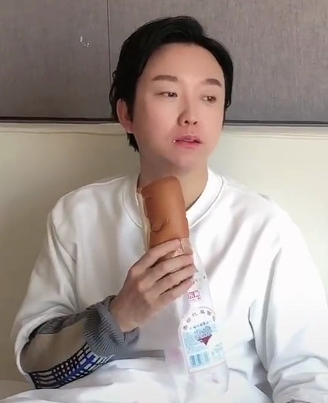 只见李玉刚半躺在床上,床上丢着一个面包,手上还拿着一个,表情呆滞地