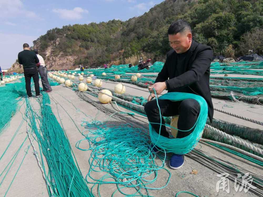 10多名漁民或站或蹲,拉線織網,一派忙碌景象.