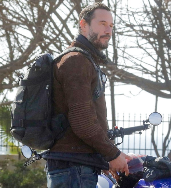 从照片中可以看到,基努·里维斯身穿棕色外套,搭配牛仔裤,背着背包,他