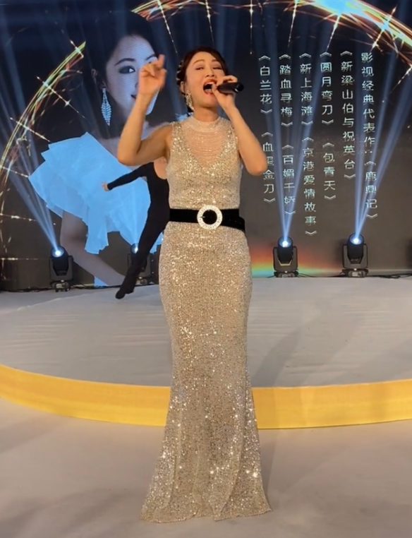 梁小冰在台上手握话筒卖力地唱歌,台下时不时传出鼓掌的声音,在她身后