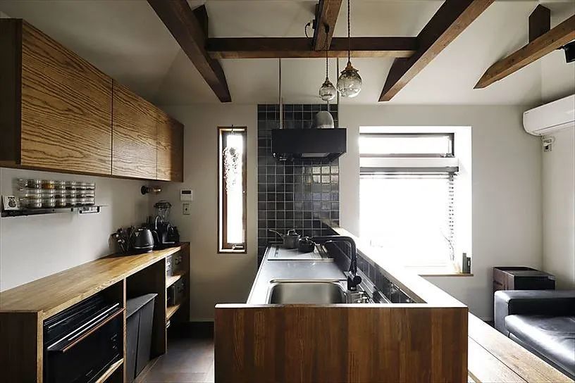 用小黑砖贴在开放式厨房区域,配合通体黑色的地柜和油烟机,让厨房的