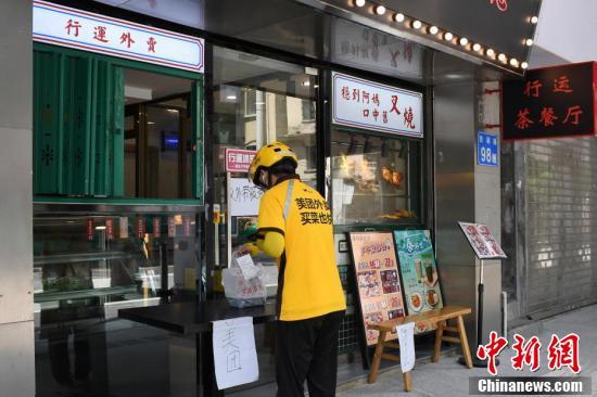 一名外卖骑手在餐饮店外取餐.一家餐饮店提示该店铺禁止堂食.
