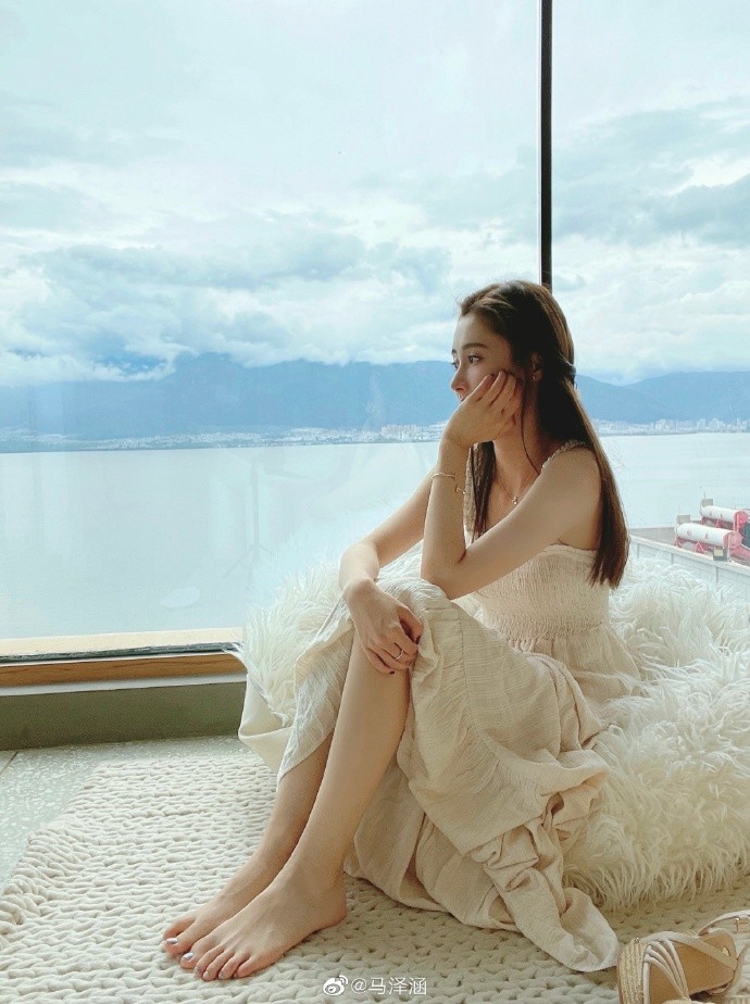 马泽涵身穿米白色露肩长裙,赤着脚,单手托腮,若有所思的样子.