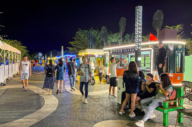 游客们坐在休闲桌椅上,眼前有美景,手中有美食,望着人群熙熙攘攘,吹着