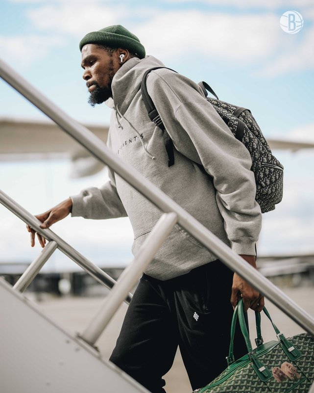 33岁杜兰特身穿黑色运动裤和灰色连帽卫衣,戴着一顶绿色针织帽,这款