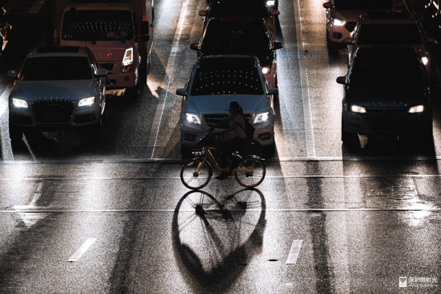 车灯照射下,共享单车的影子在雨后的路面上,倒映出了一颗"爱心"//愿你