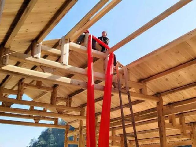 在上梁时,工人会用绳子绑住房梁的两端,一批人站在墙上拉,一批人站在