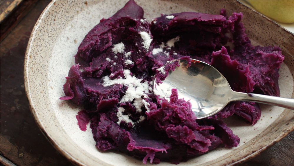 3,紫薯取出来以后,趁热加上一勺糖粉,用勺子压成紫薯泥.