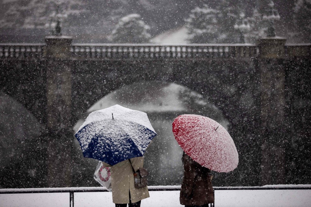 1月6日,人们在日本东京街头打伞冒雪出行