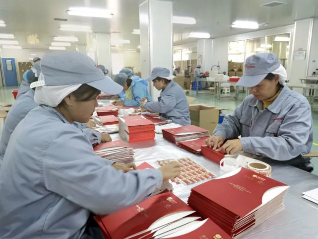 包装车间组长罗艳带领小组成员正在给礼盒贴标签,标签上印有"2022中央