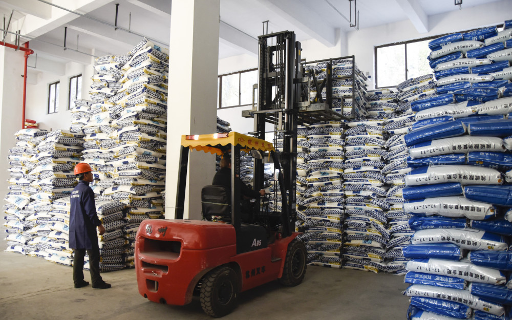 有限公司,一辆满载农资的货车正在卸货,叉车不断出入仓库,将化肥整齐