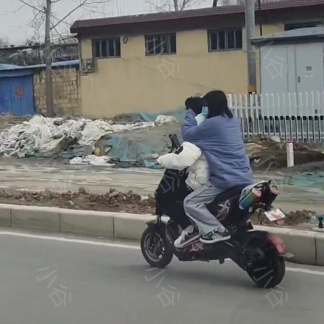 男孩騎電動車帶著女孩,女孩怕男孩耳朵冷用手捂著,年輕真好