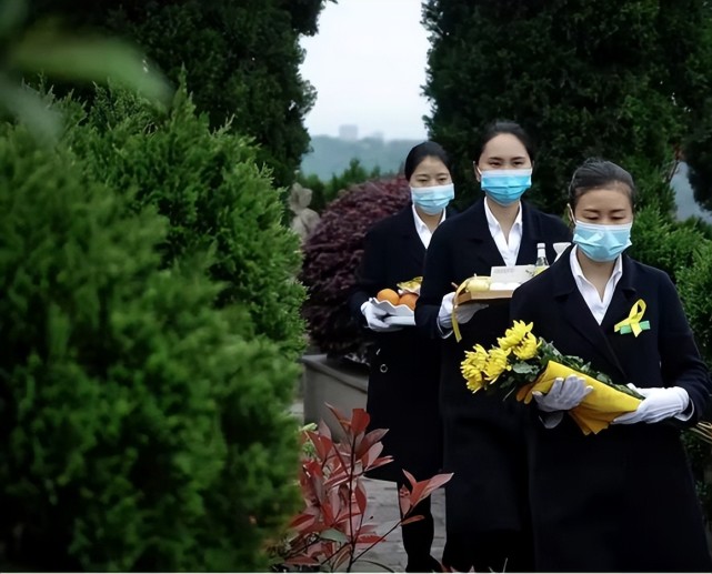 礼仪师手持鲜花,水果,糕点等祭扫用品.