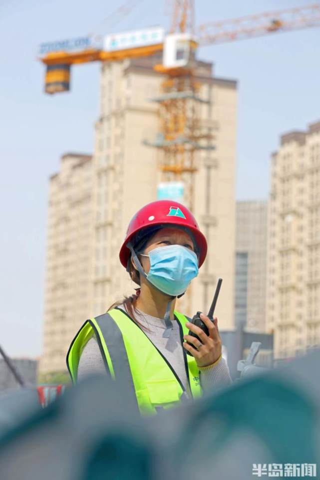 "塔吊信号工陈泉妹手持着对讲机正指挥着塔吊工作,巨大的塔吊在她的