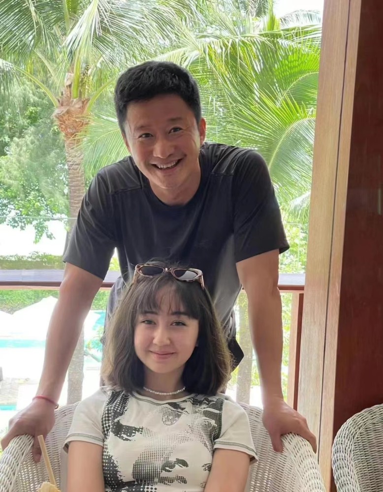照片里吴京站在蔡书雅身后,留着寸头,穿着简单的黑色t恤,手撑着藤椅