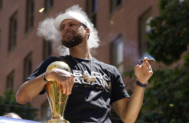 库里抱着全明星赛mvp,西决mvp和fmvp三座奖杯参加庆典,抽雪茄时露出