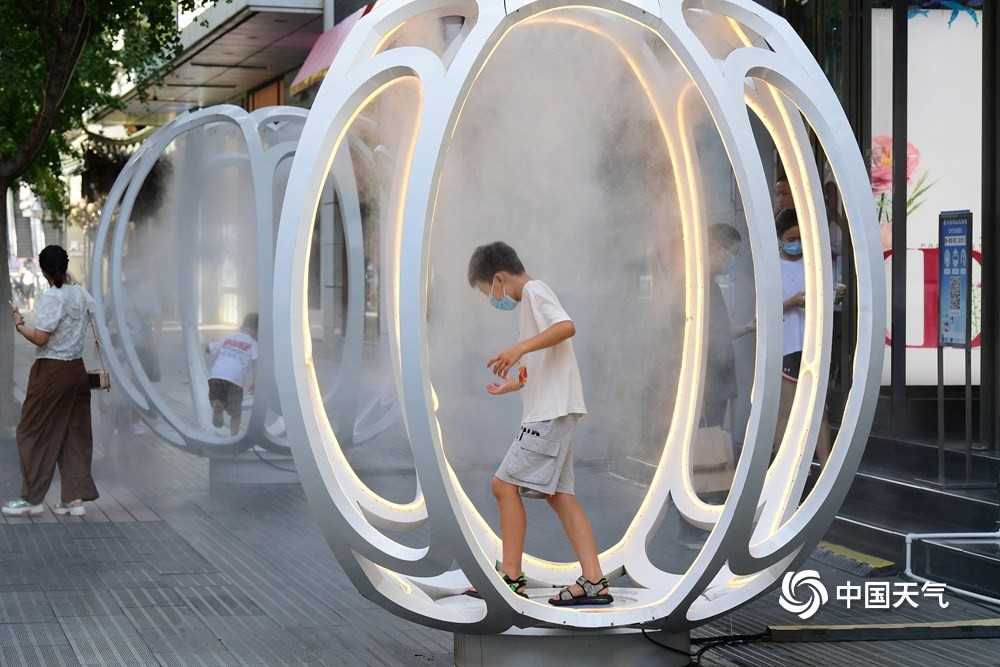 着白色雾气的装置前嬉戏拍照,乐享高温热浪下"雾森"系统带来的凉爽