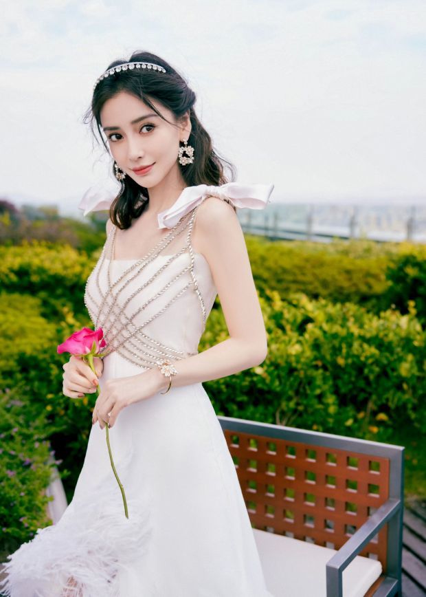 照片中的杨颖身穿白色长裙,长发披肩搭配银色发卡,手拿鲜花好似花仙子