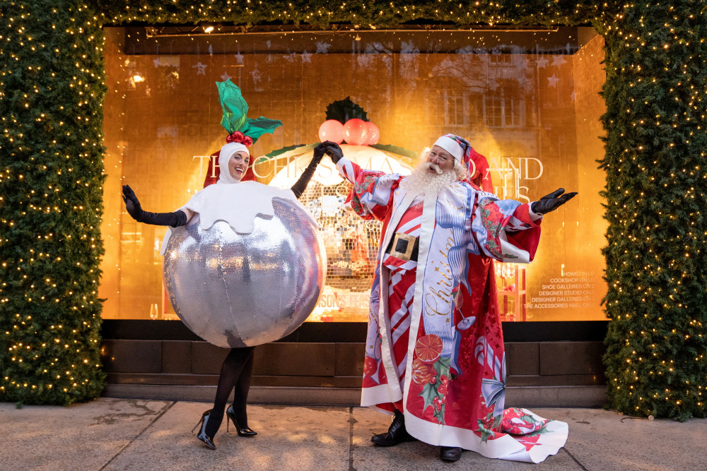 身着圣诞风格服饰的表演者在英国伦敦一处商场的圣诞橱窗前表演
