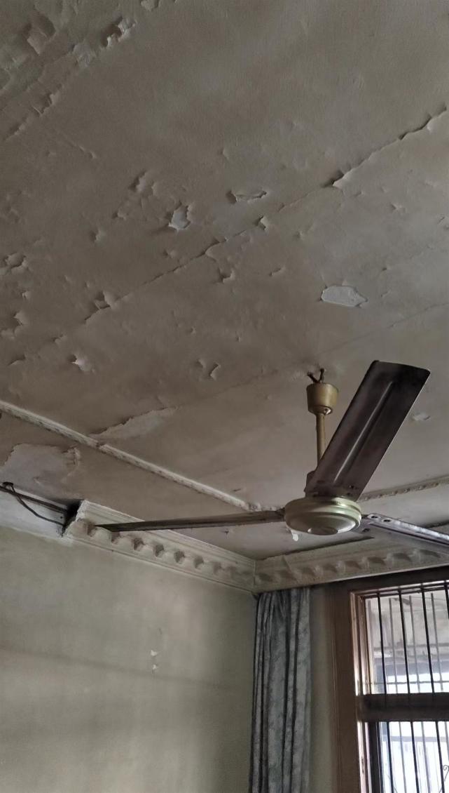 天花板墙角的石膏条断裂,露出黑色的电线;老式的吊扇,日光灯,片片脱落