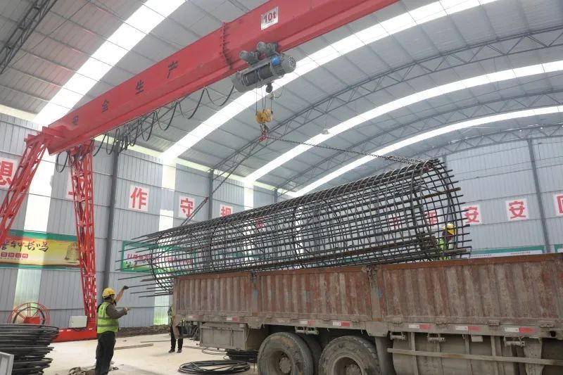 在钢筋加工棚内,工人正在进行桩基钢筋笼制作,大家配合娴熟将桩基钢筋