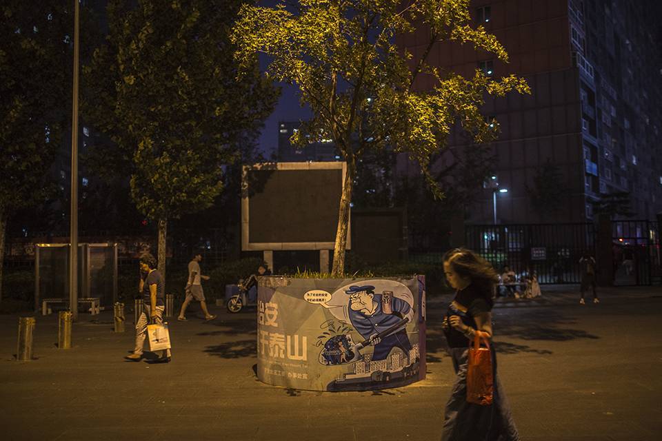 夜晚，行人匆匆走过像素小区的大街，树木被小区的宣传标语包裹着。