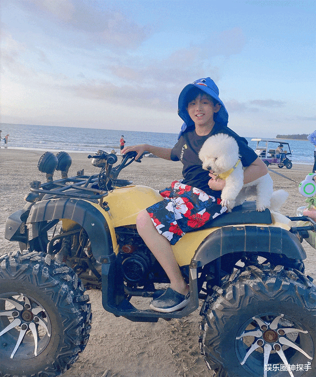 张艺瀚曾带狗狗在海边玩耍,他身穿花短裤,头戴蓝色帽子,怀中抱着狗狗
