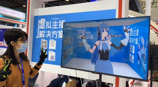 图片展示一位戴眼镜的女士与电视屏幕中的虚拟动漫角色互动，屏幕旁边有中文文字和二维码。