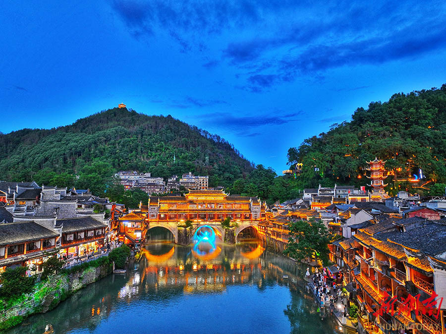 游客在灯火辉煌的凤凰古城中漫游沱江,打卡留念,体验中国最美小城