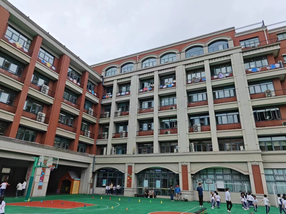 操场上,一群小学生在体育老师的指引下,仰头对着教学楼"东张西望".