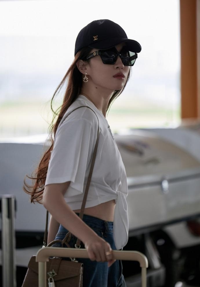 全身照中,刘亦菲打扮清爽,拉着大牌箱包大步前行,时而微笑比v,时而胯